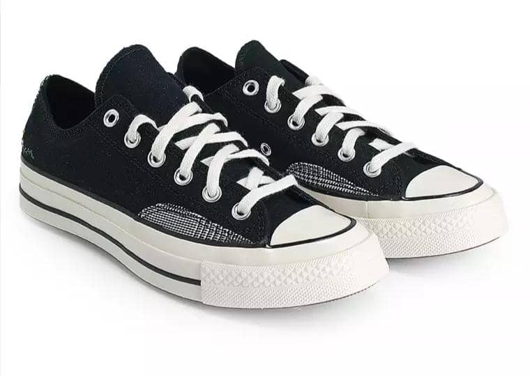 Sepasang sepatu sneakers kanvas hitam model low-cut dengan sol karet putih dan tali sepatu putih bergaya klasik.