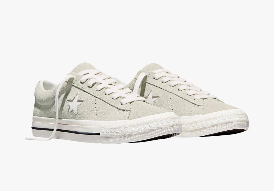 Sepasang sepatu sneakers berwarna abu-abu muda dengan tali putih dan logo bintang di sisi, bergaya kasual dan minimalis.