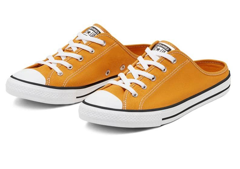 Sepasang sepatu slip-on kanvas berwarna oranye dengan tali putih dan sol karet putih bergaris hitam bergaya kasual.