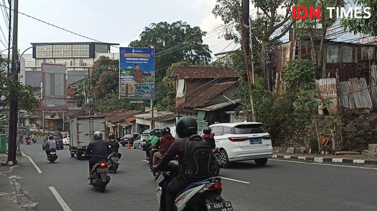 Pemotor dan mobil melintas di turunan Jalan Gombel Lama dengan deretan rumah dan papan reklame di sisi jalan.