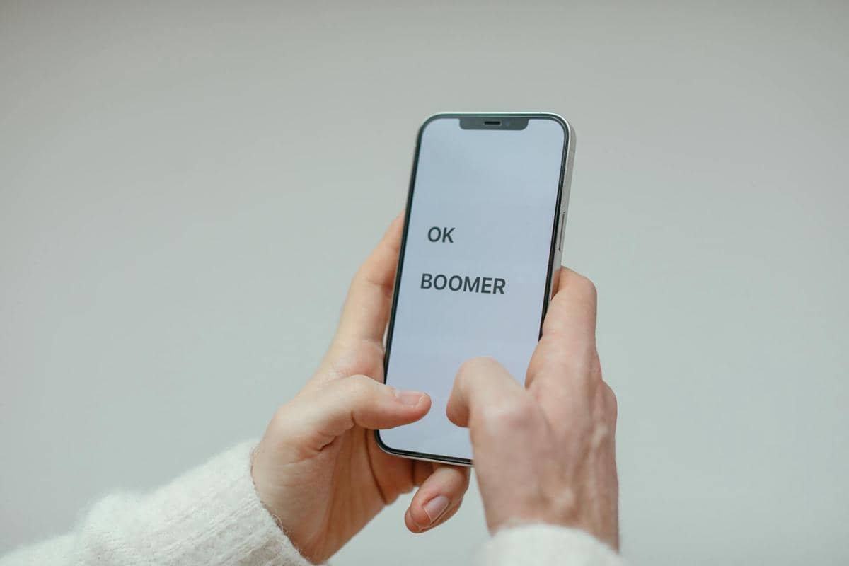 Seseorang memegang ponsel dengan layar menampilkan tulisan 'OK BOOMER' dalam huruf besar di latar putih.