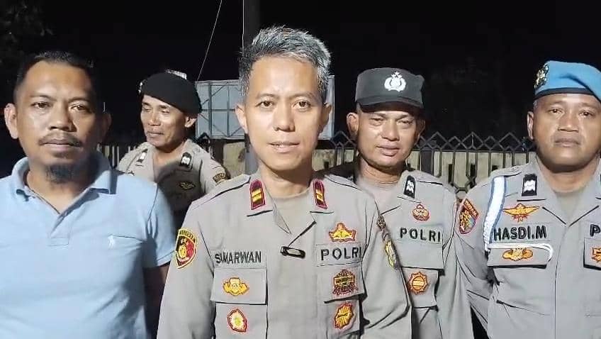 Beberapa anggota kepolisian berdiri bersama di area luar pada malam hari mengenakan seragam lengkap dengan atribut kepolisian.