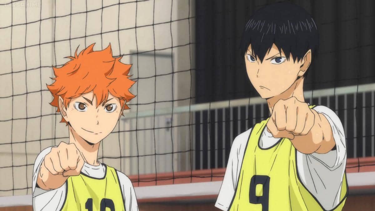 Hinata dan Kageyama mengenakan rompi latihan bernomor di lapangan voli dengan ekspresi serius dan tangan mengepal ke depan.