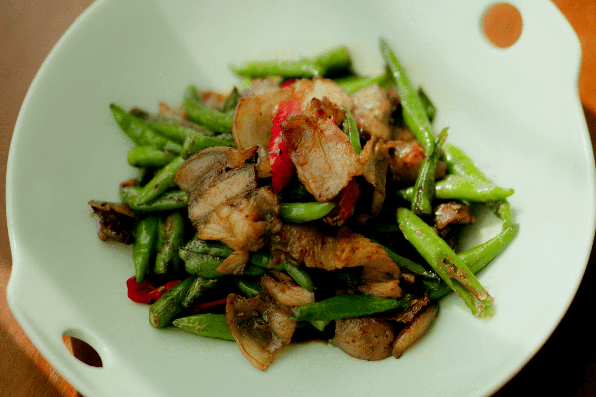Tumis ayam buncis dengan irisan cabai merah dan potongan daging ayam disajikan di atas piring putih berbentuk bundar.