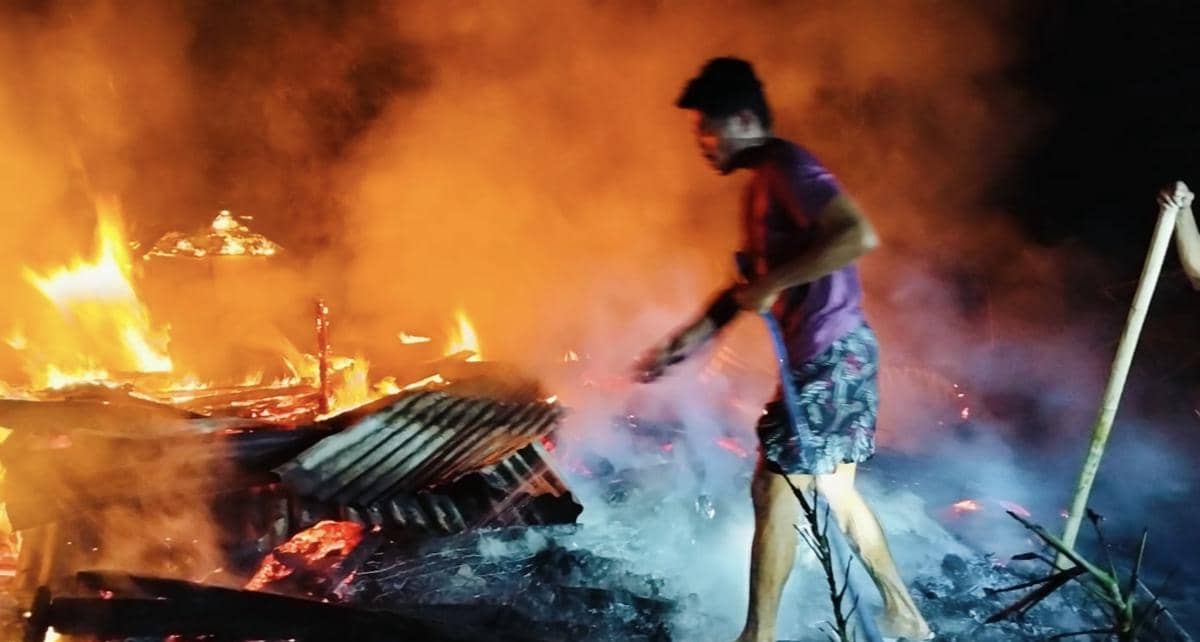 Seorang pria berusaha memadamkan api di lokasi kebakaran rumah di Nagekeo, NTT, dengan kobaran api besar dan asap tebal di malam hari.