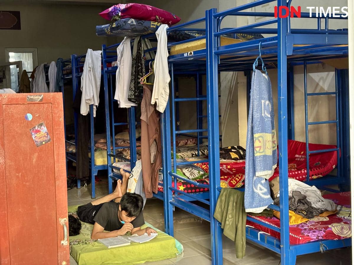 Seorang santri membaca buku sambil berbaring di lantai kamar asrama dengan deretan ranjang susun berwarna biru di Pondok Pesantren Muhammadiyah Kudus.