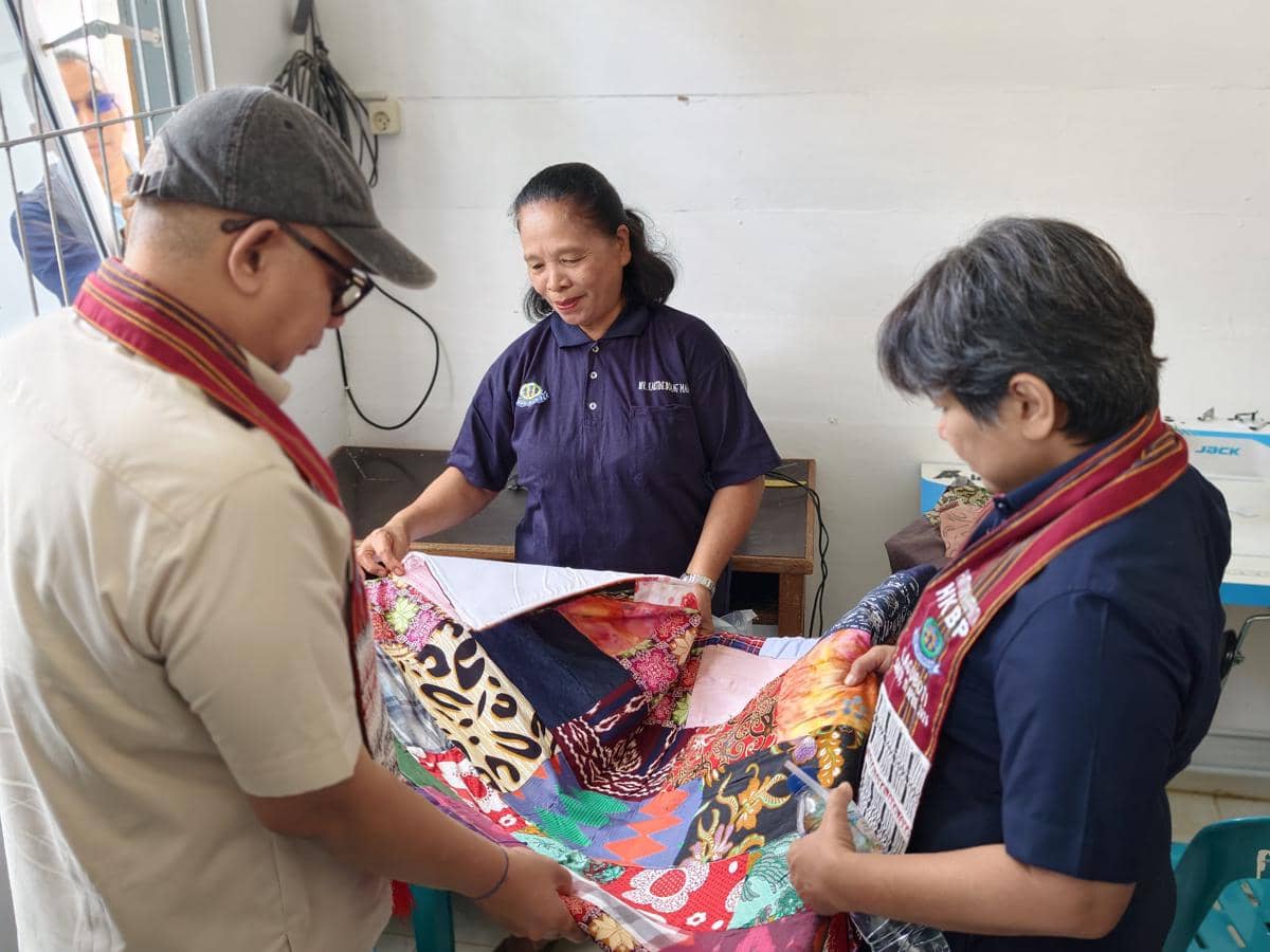 Tiga orang mengenakan pakaian kerja sedang melihat kain batik berwarna-warni dalam kegiatan CSR PT Inalum di Paritohan.