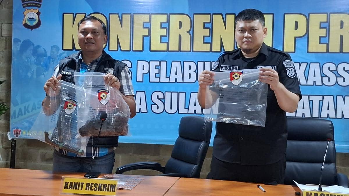 Dua petugas Polres Pelabuhan Makassar memperlihatkan barang bukti berupa senjata tajam dan pakaian korban dalam konferensi pers.