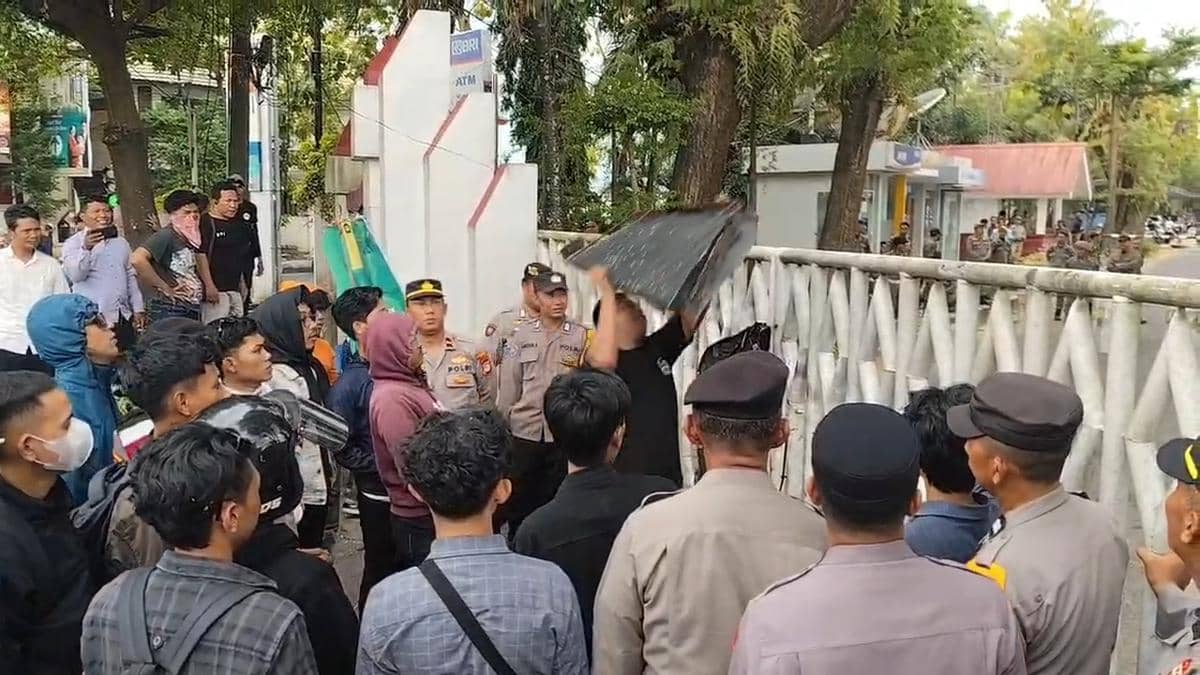 Sejumlah massa dari Pormula berunjuk rasa di depan Kantor Bupati Gowa sambil berhadapan dengan aparat kepolisian yang berjaga.