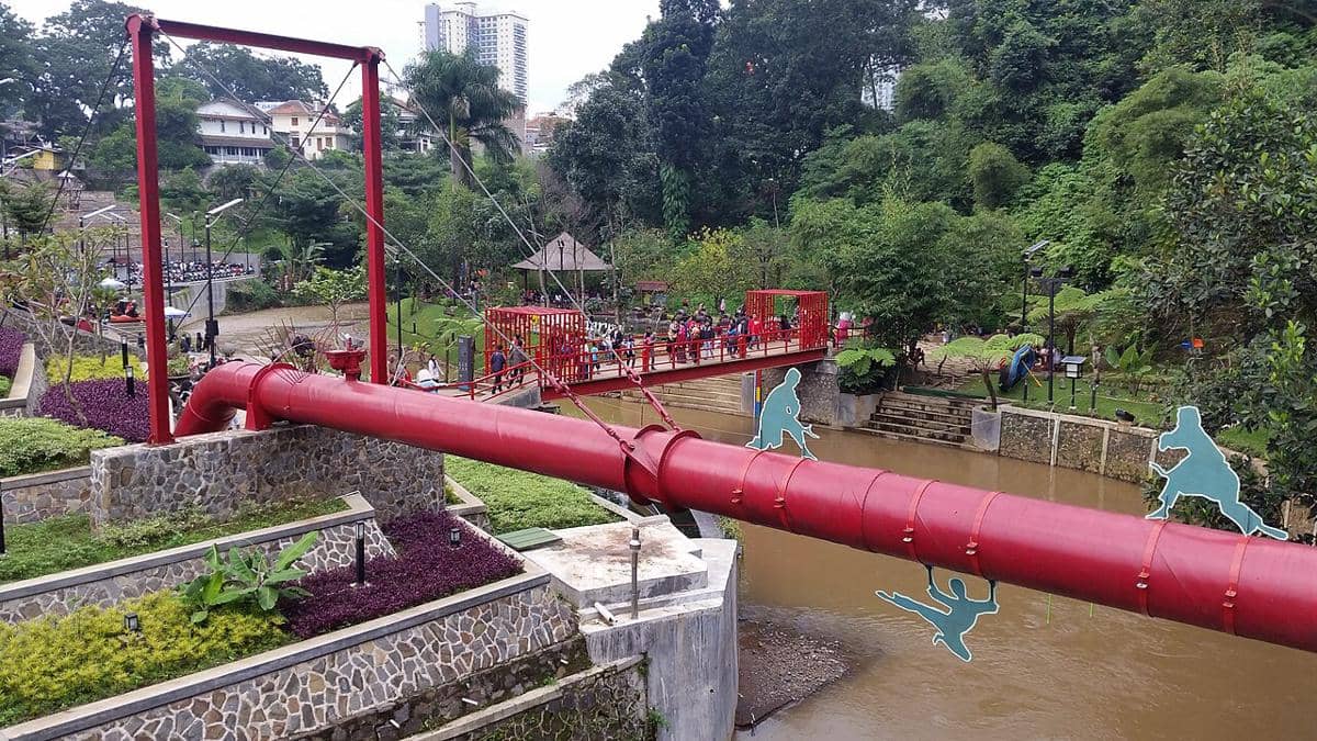 Pemandangan Teras Cikapundung di Bandung dengan jembatan merah di atas sungai, dikelilingi taman hijau dan pengunjung yang berjalan santai.