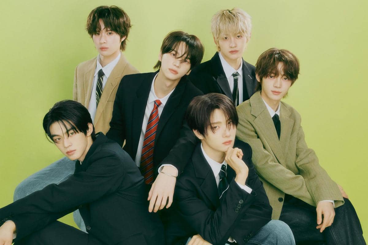 Enam anggota grup TWS berpose mengenakan setelan jas dan dasi dengan latar belakang hijau lembut bergaya formal dan modern.