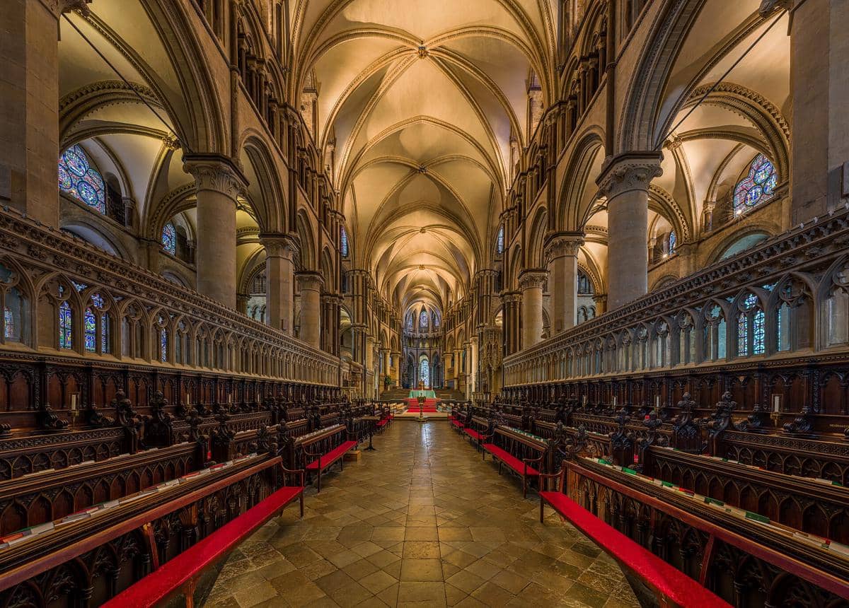 Deretan bangku paduan suara berhias ukiran kayu di Katedral Canterbury menghadap Kapel Trinitas yang bercahaya.