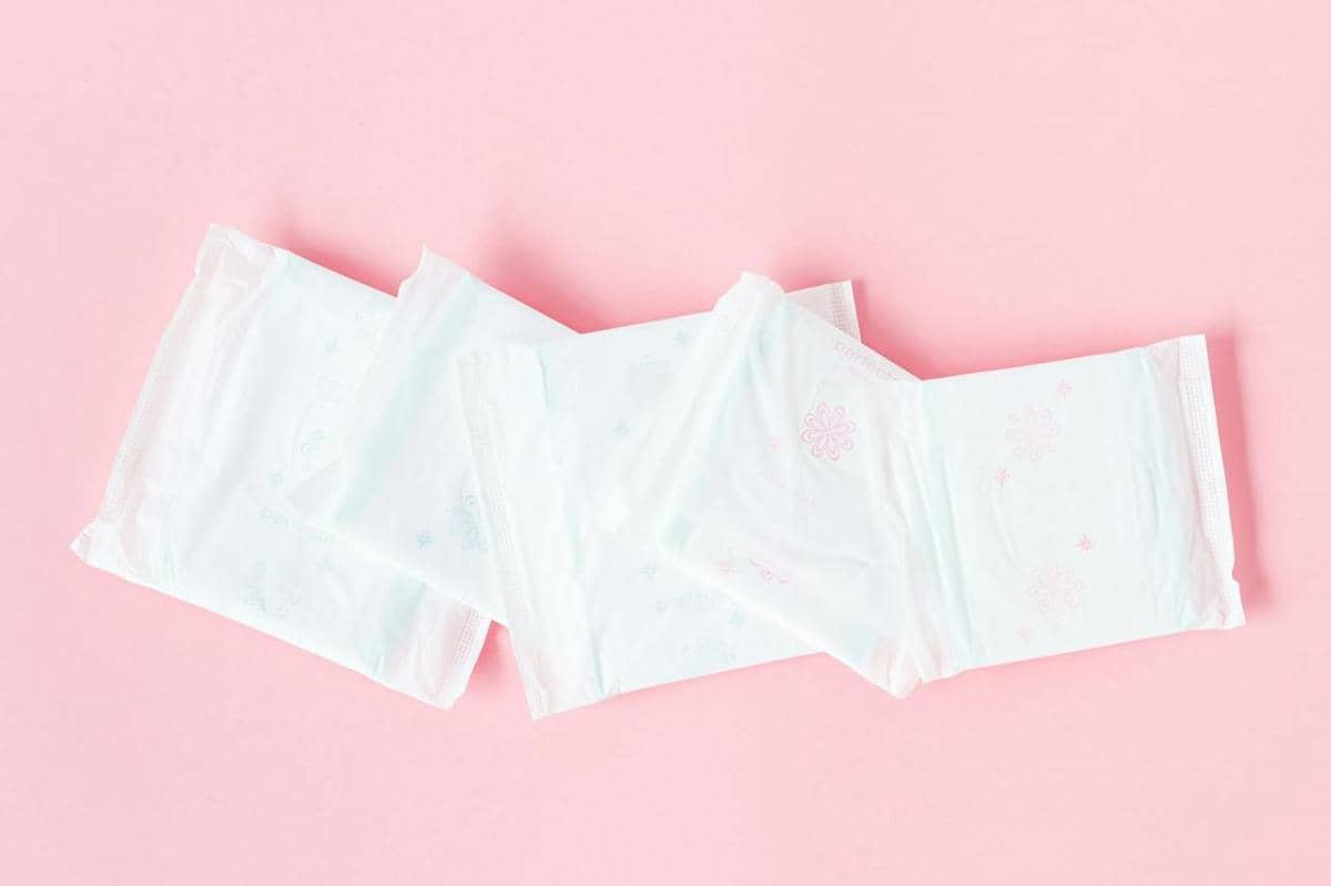 Beberapa pantyliner berwarna putih dalam kemasan tergeletak di atas permukaan berwarna merah muda lembut.