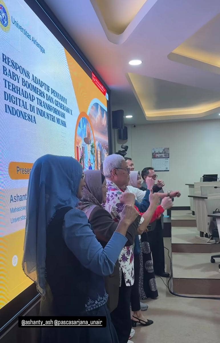 Beberapa orang berdiri di depan layar presentasi besar bertuliskan topik tesis tentang transformasi digital di industri musik Indonesia di Universitas Airlangga.