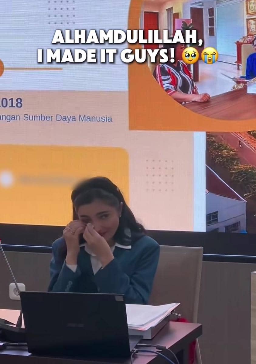 Seorang wanita mengenakan jas biru duduk di depan laptop sambil menyeka air mata saat sidang disertasi S3 di UNAIR Surabaya.