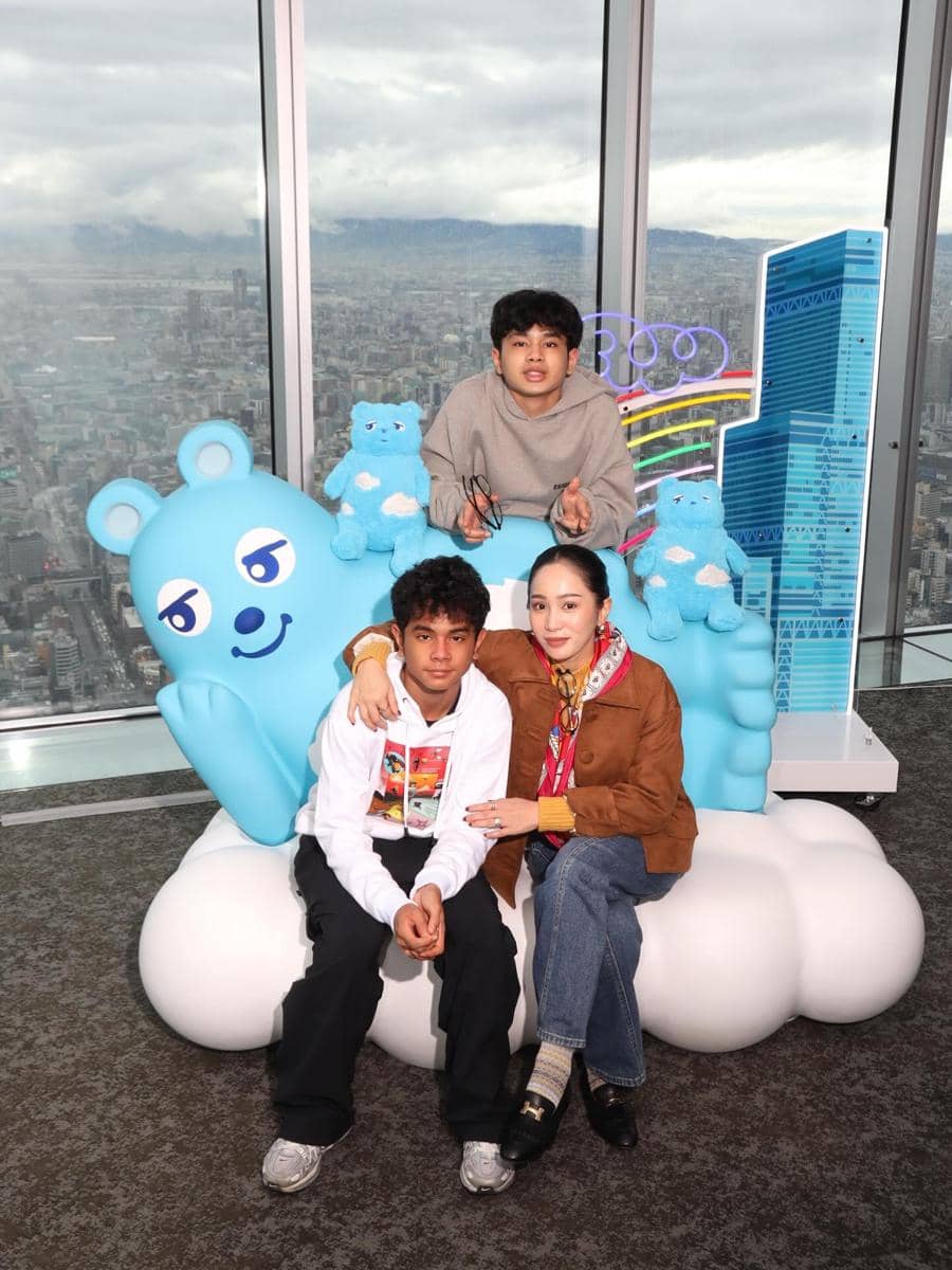 Bunga Zainal dan anak-anaknya berpose di area observasi gedung tinggi dengan latar kota dan dekorasi boneka beruang biru.