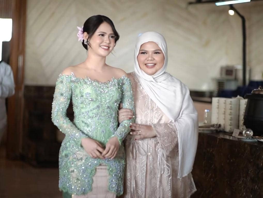 Maizura tersenyum berdiri berdampingan, satu mengenakan kebaya hijau muda berhias payet dan satu lagi memakai hijab putih krem.