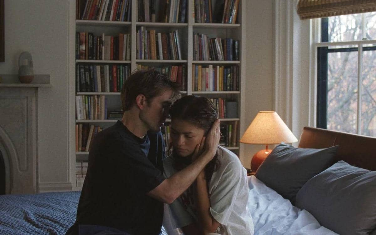 Seorang pria memeluk wanita dengan lembut di kamar tidur yang diterangi lampu meja, dengan rak buku besar di latar belakang.