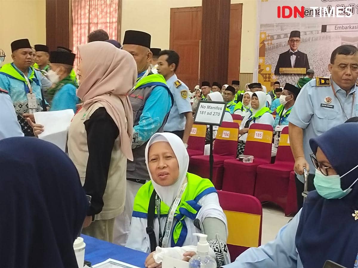 Calon jemaah haji kloter pertama tiba di Embarkasi Medan, duduk dan berinteraksi dengan petugas sambil menunggu proses keberangkatan.