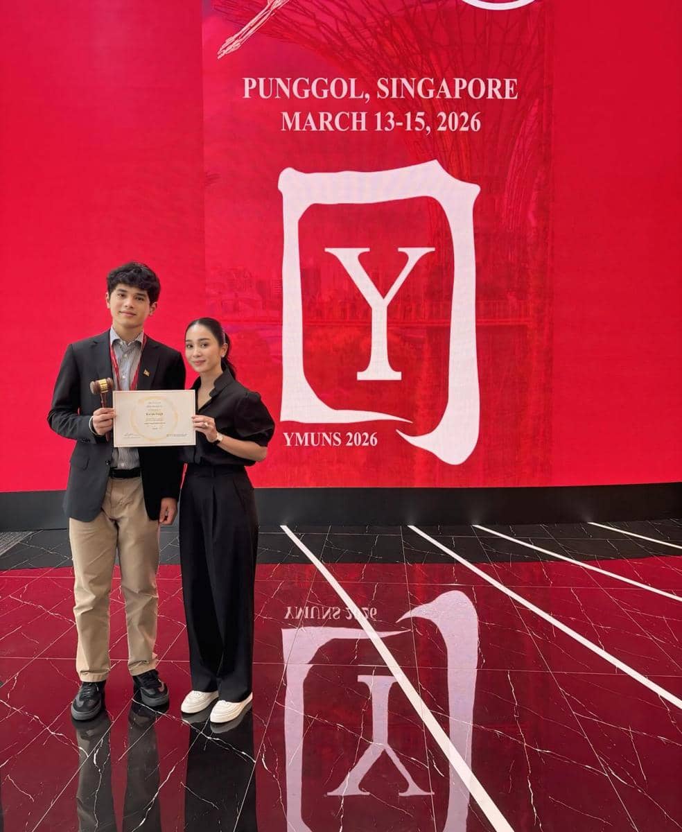 Bunga dan anaknya berdiri di depan latar merah bertuliskan Punggol, Singapore, Maret 2026, sambil memegang sertifikat dan palu penghargaan.