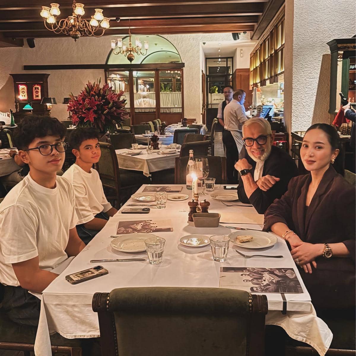 Keluarga Bunga Zainal duduk bersama di meja makan restoran elegan dengan pencahayaan hangat dan suasana klasik yang nyaman.