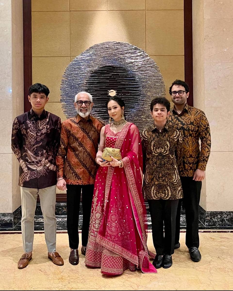 Keluarga Bunga Zainal berpose bersama di depan dinding dekoratif, mengenakan busana formal dengan nuansa batik dan gaun tradisional merah.