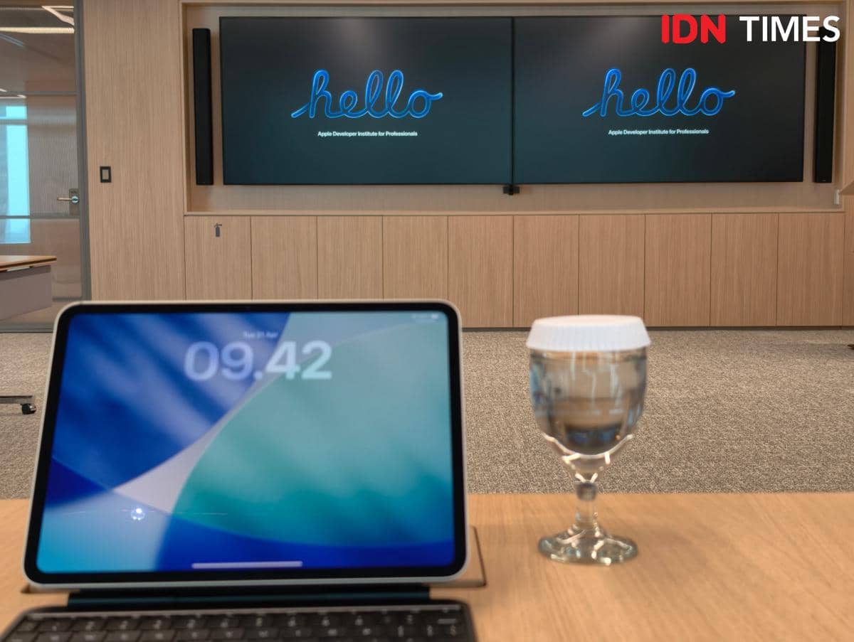 Ruang kelas Apple Developer Institute di Jakarta dengan layar besar bertuliskan hello dan tablet di atas meja bersama segelas air.