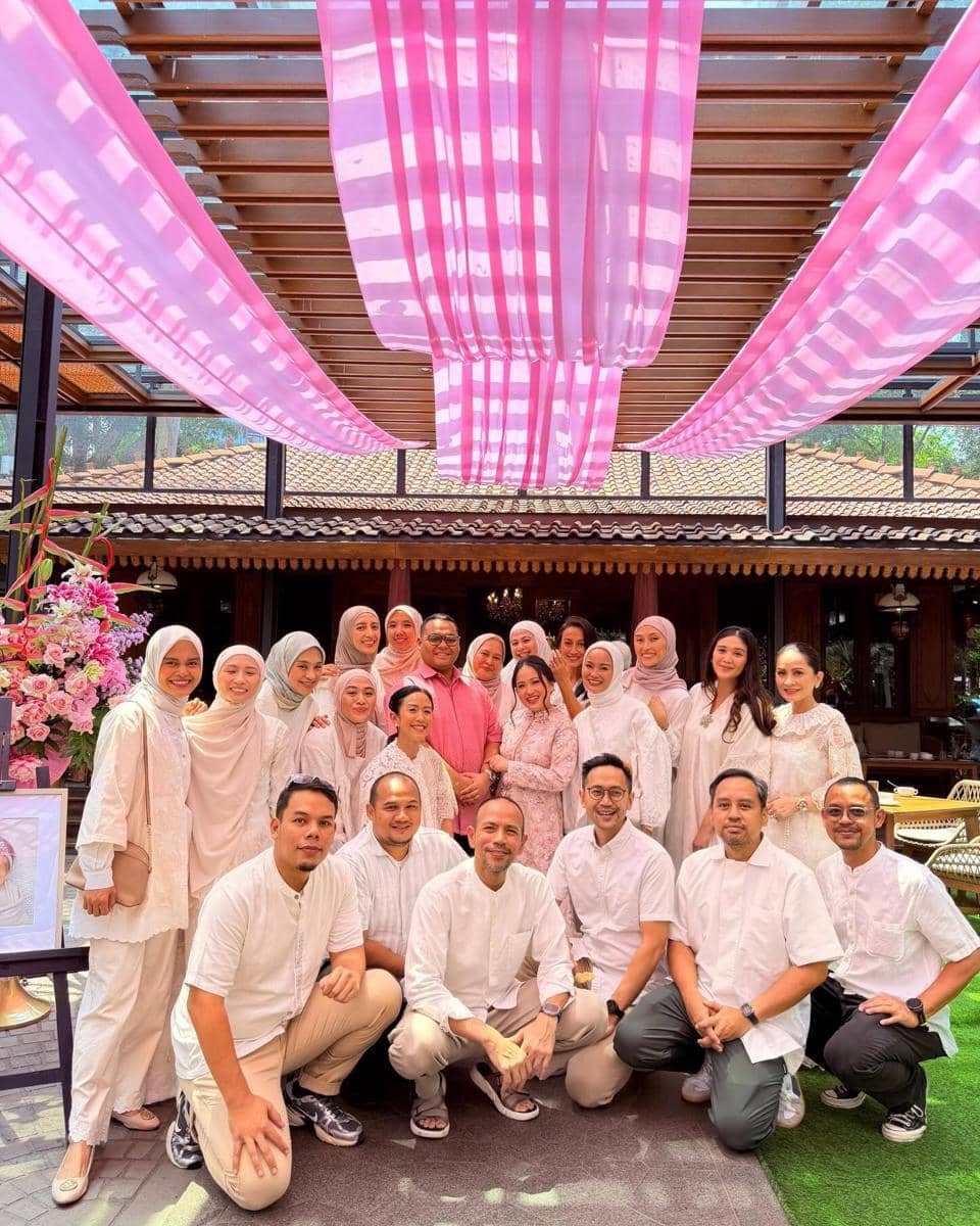Sekelompok orang berpose bersama dalam acara akikah dengan dekorasi kain berwarna merah muda dan putih di area terbuka beratap kayu.