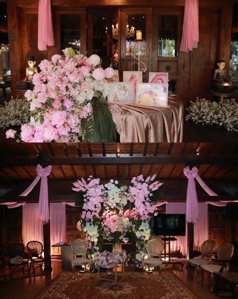 Dekorasi acara akikah dengan nuansa bunga berwarna pink dan putih, dihiasi kain satin serta pencahayaan hangat di ruangan kayu.