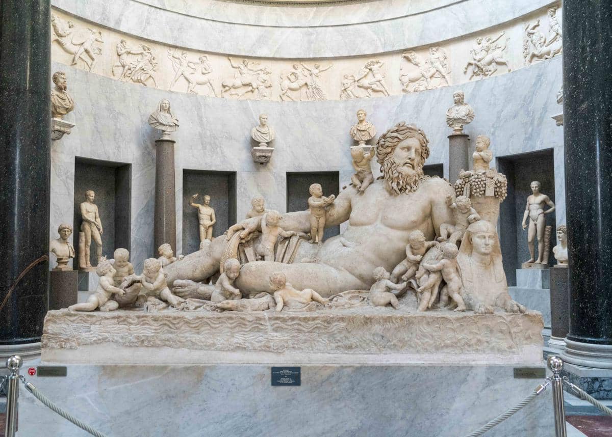 Patung marmer besar bergaya klasik di Museum Vatikan menampilkan sosok pria berjanggut dikelilingi anak-anak kecil dan relief di dinding belakang.