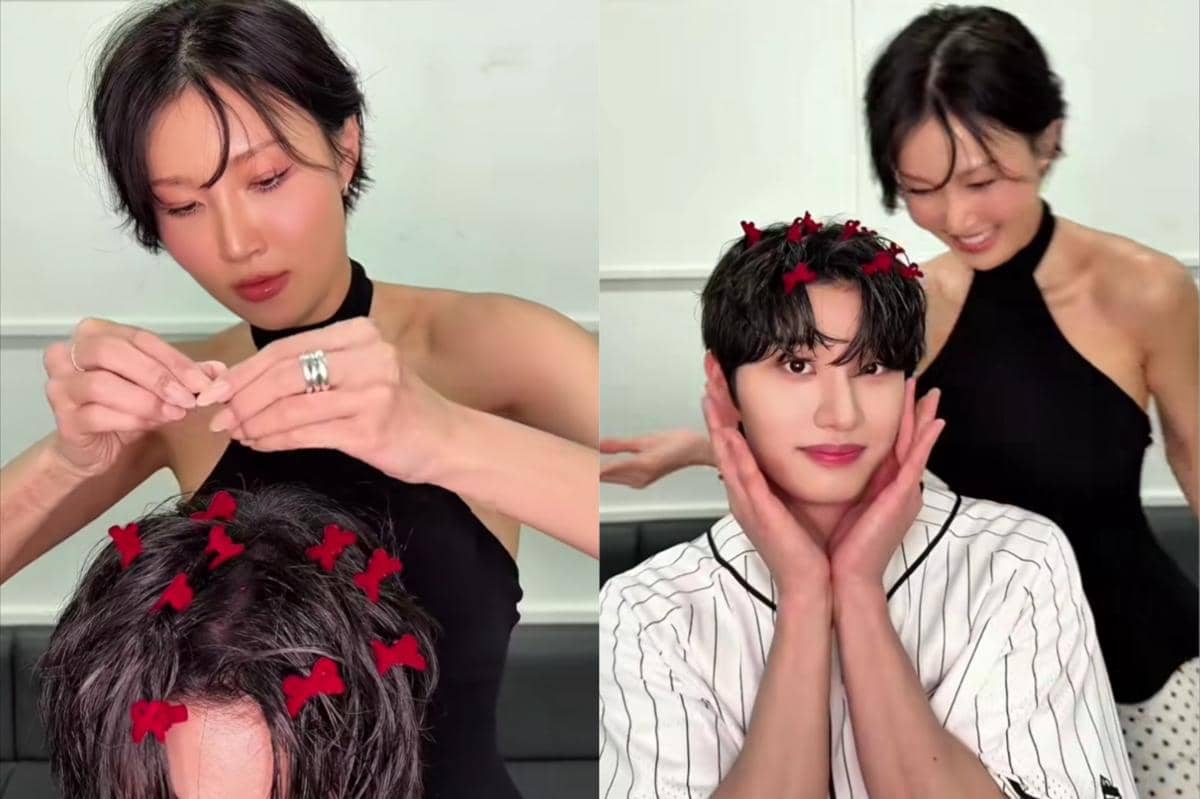 Seorang wanita mengenakan gaun hitam tanpa lengan menata rambut pria dengan jepit pita merah kecil, keduanya tersenyum di ruangan terang.