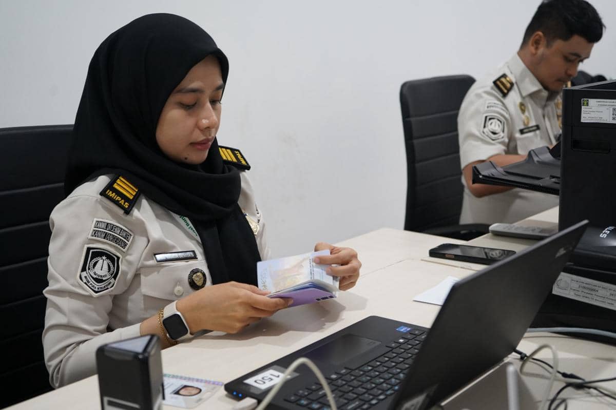 Petugas Imigrasi Tangerang memeriksa paspor di meja kerja dengan komputer dan dokumen untuk layanan jemaah haji Embarkasi Cipondoh.