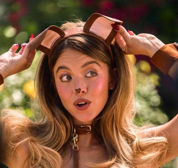 Sydney Sweeney mengenakan aksesori telinga anjing dan kalung cokelat dengan latar taman yang cerah.