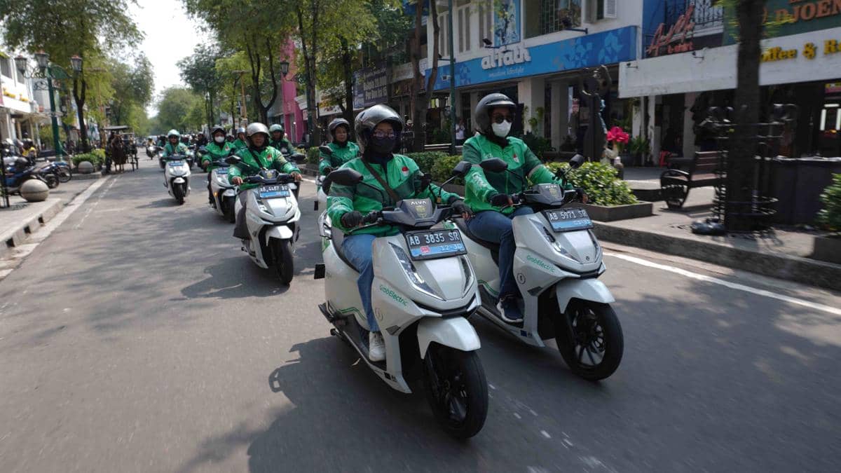 Sejumlah pengemudi ojek online mengendarai motor listrik berwarna putih melintasi jalan kota Yogyakarta dengan mengenakan jaket hijau dan helm.