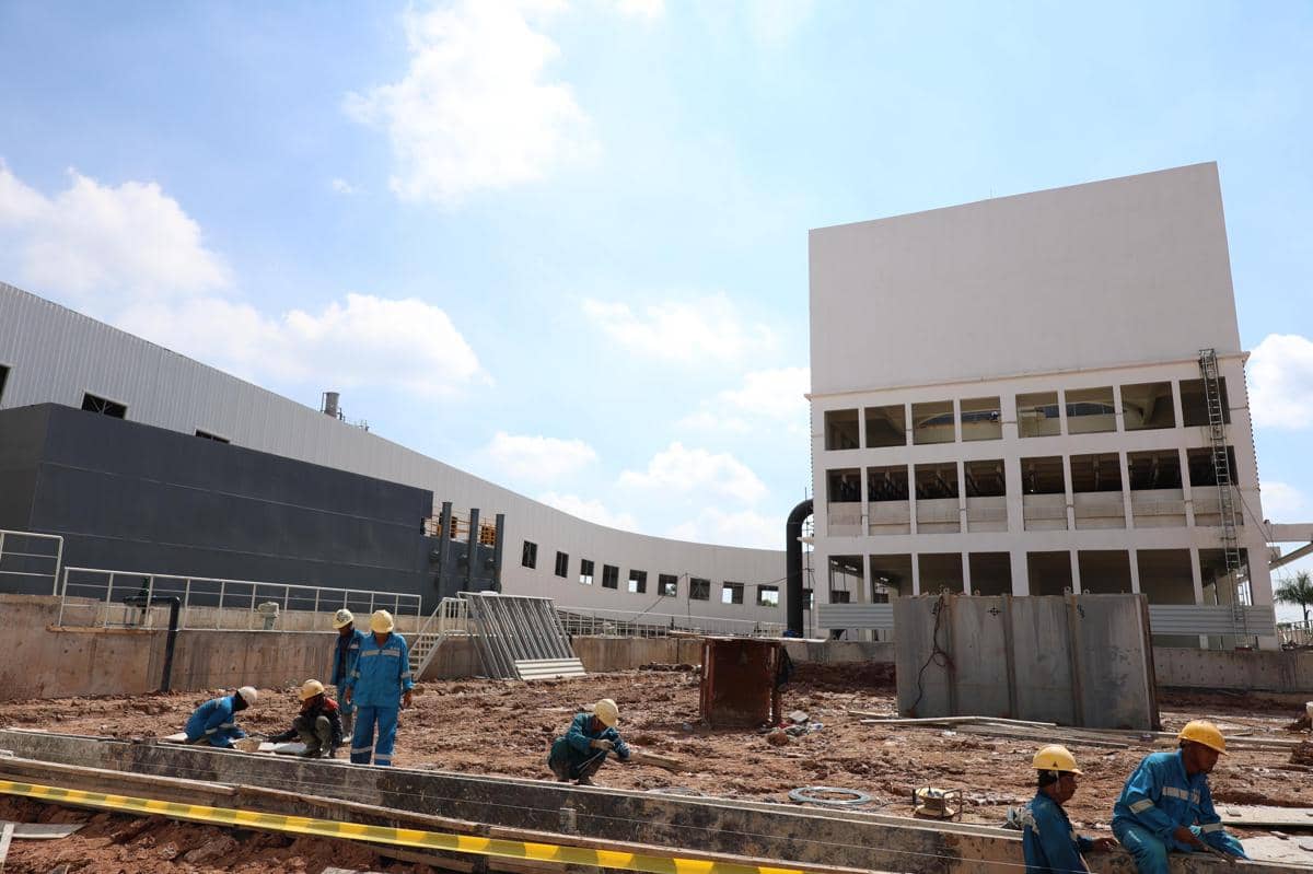Pekerja konstruksi dengan helm keselamatan sedang membangun fasilitas PSEL Keramasan Palembang di bawah langit cerah.