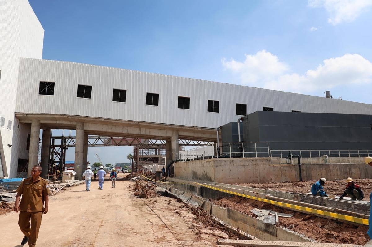 Pekerja dan petugas berada di area pembangunan fasilitas PSEL Keramasan Palembang dengan bangunan besar berwarna putih di bawah langit cerah.