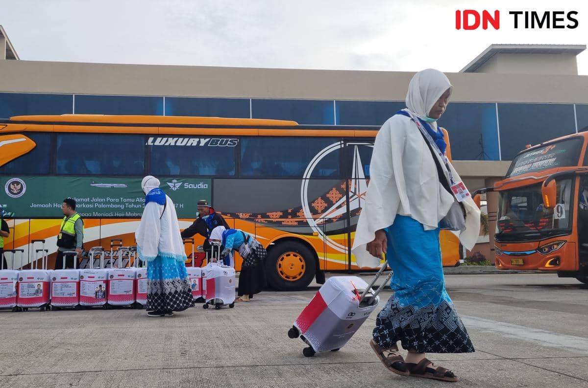 Jemaah haji kloter pertama Embarkasi Palembang berjalan membawa koper menuju bus oranye sebelum keberangkatan ke Tanah Suci.