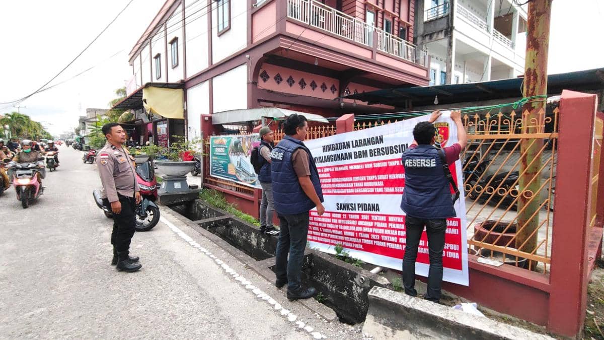 Petugas Polda Riau memasang spanduk berisi larangan penyalahgunaan BBM bersubsidi di pagar rumah di tepi jalan kawasan permukiman.