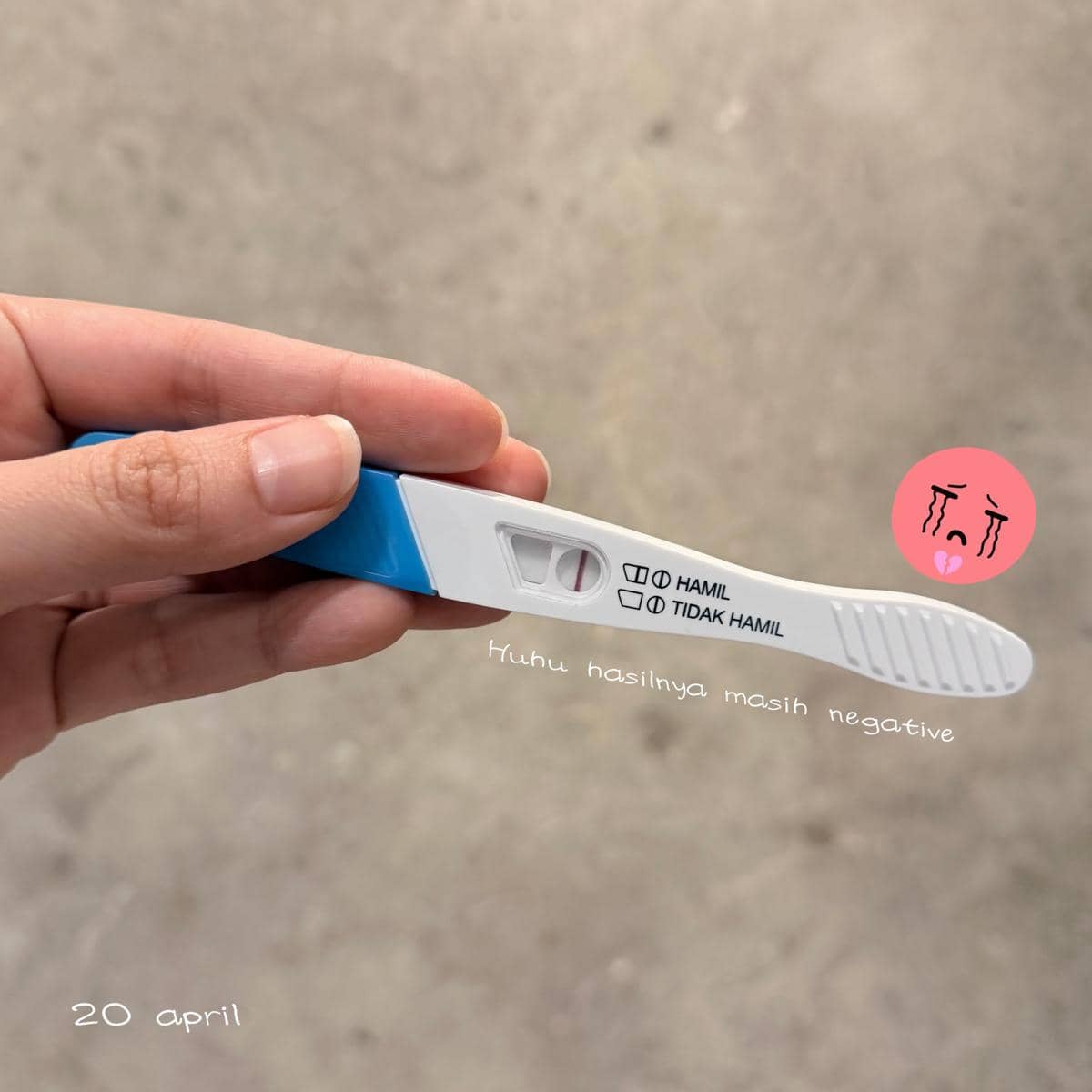 Tangan memegang alat tes kehamilan dengan hasil satu garis yang menunjukkan hasil negatif di latar abu-abu.