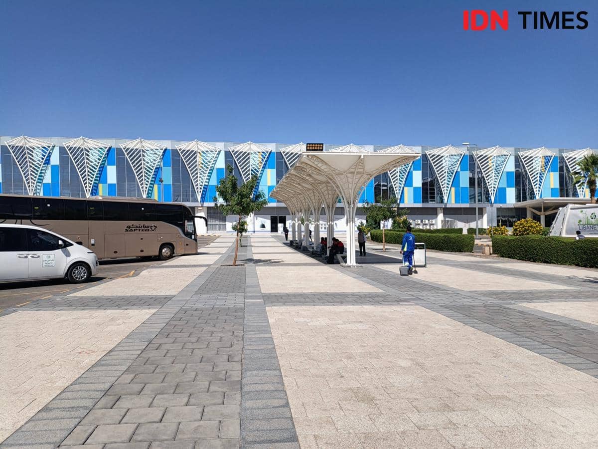 Area pemberhentian bus untuk jemaah jalur fas track dengan bangunan modern bercorak biru di latar belakang pada siang hari.