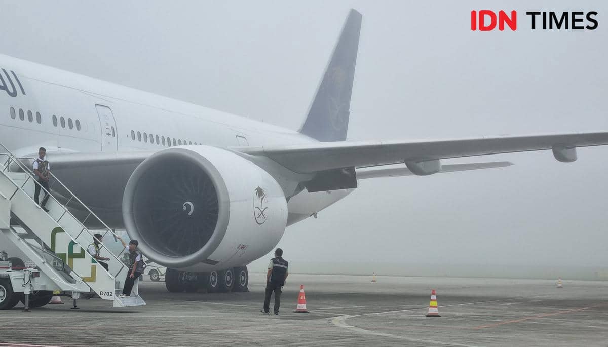 Pesawat penumpang besar berada di landasan Bandara SMB II Palembang yang diselimuti kabut tebal dengan beberapa petugas di sekitarnya.