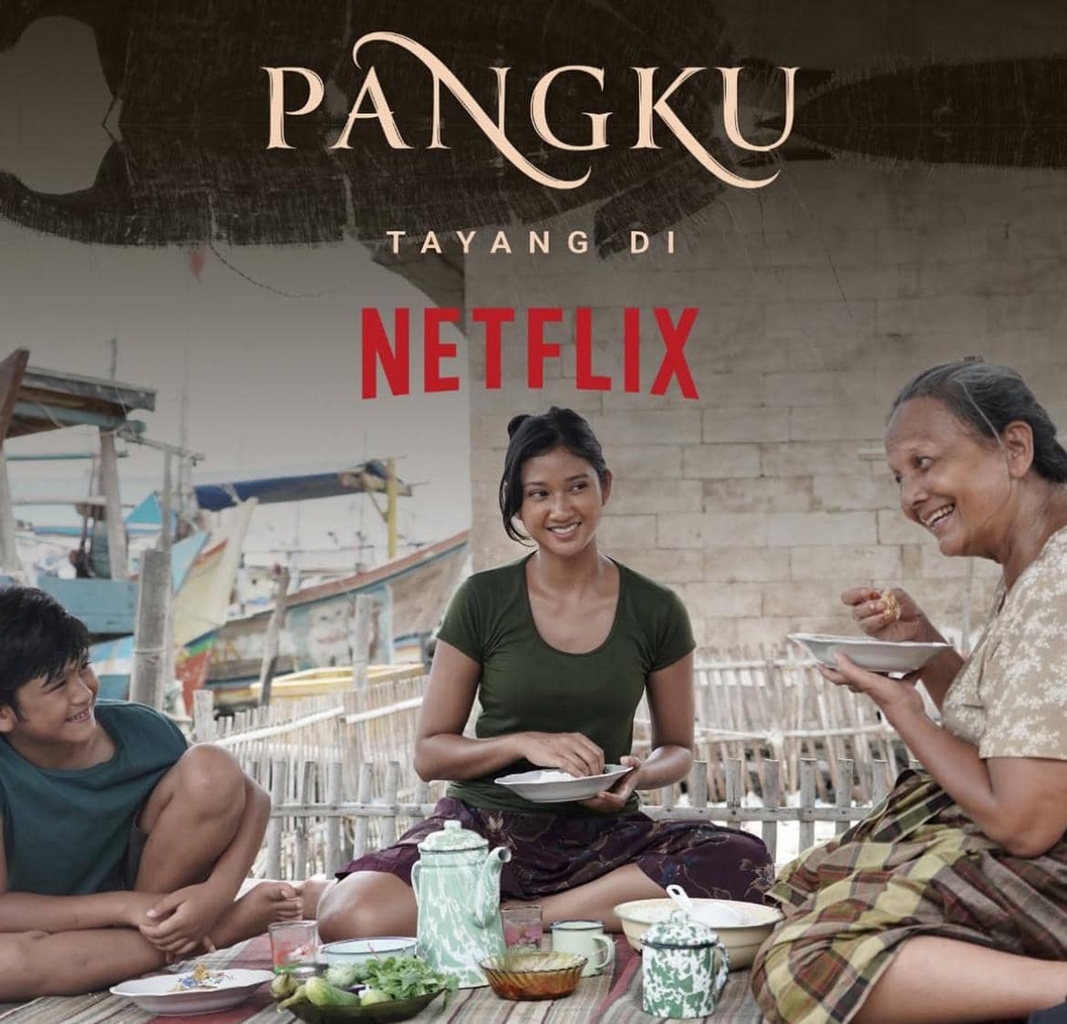 Tiga orang duduk bersama di luar rumah sambil menikmati makanan tradisional, dengan tulisan film Pangku tayang di Netflix di atas mereka.