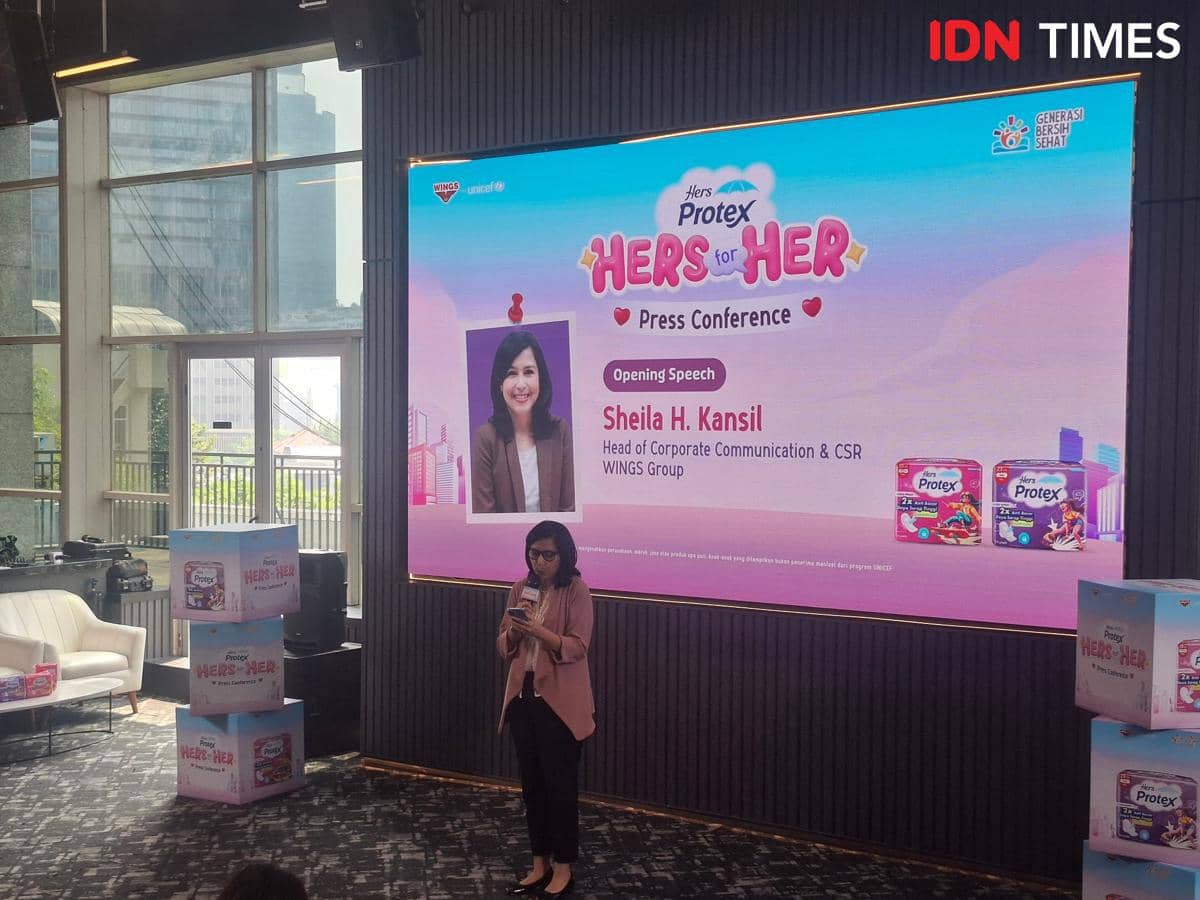 Seorang pembicara memberikan sambutan di konferensi pers Hers Protex CSR Program di Jakarta Selatan dengan layar besar di belakangnya.