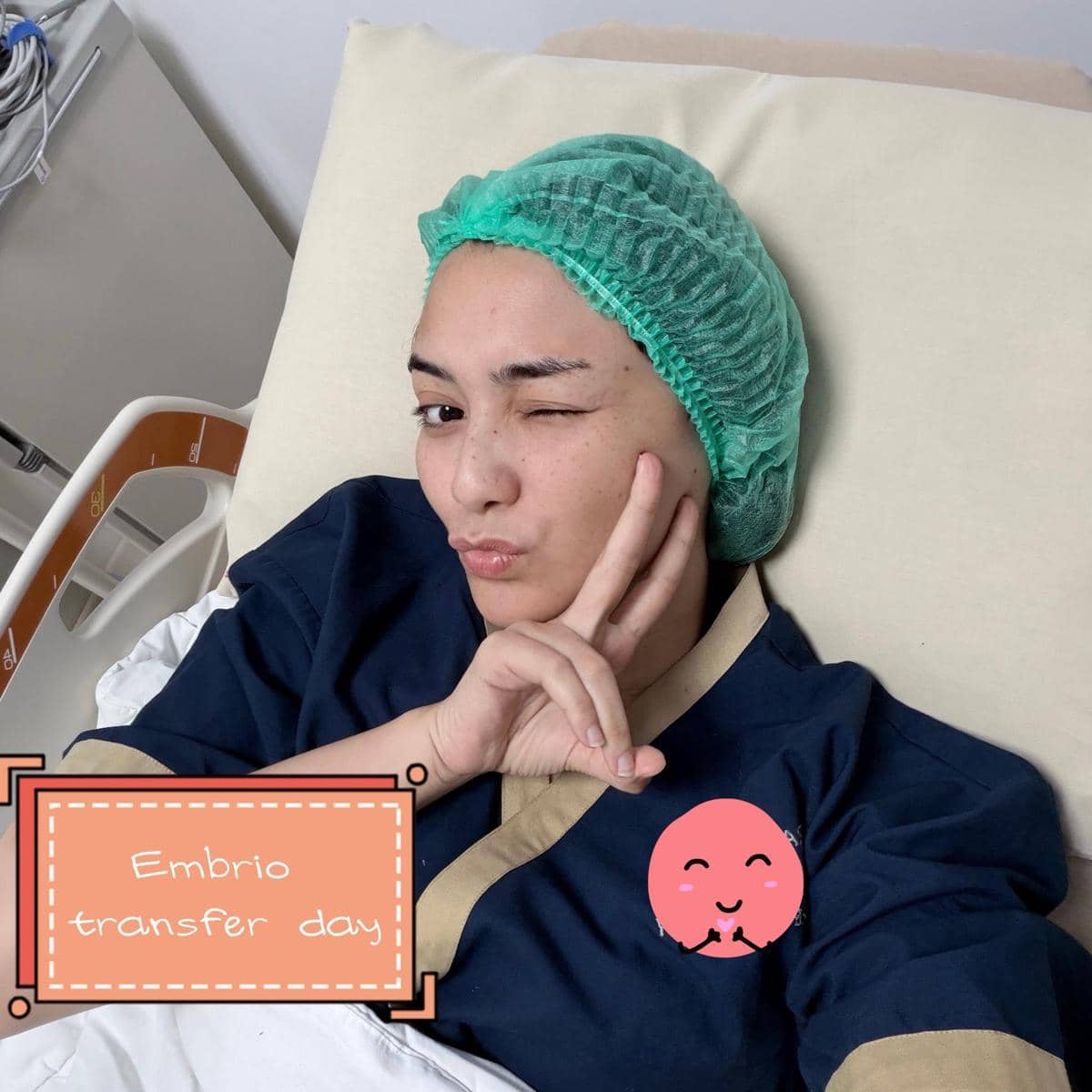 Citra Kirana di ranjang rumah sakit mengenakan pakaian pasien dan penutup kepala hijau dengan tulisan 'Embrio transfer day'.