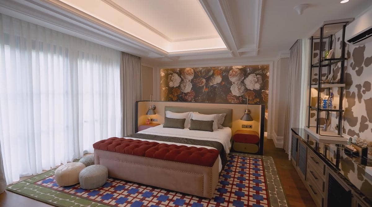 Kamar tidur mewah dengan tempat tidur besar, dinding bermotif bunga, pencahayaan lembut, dan dekorasi modern berwarna hangat.