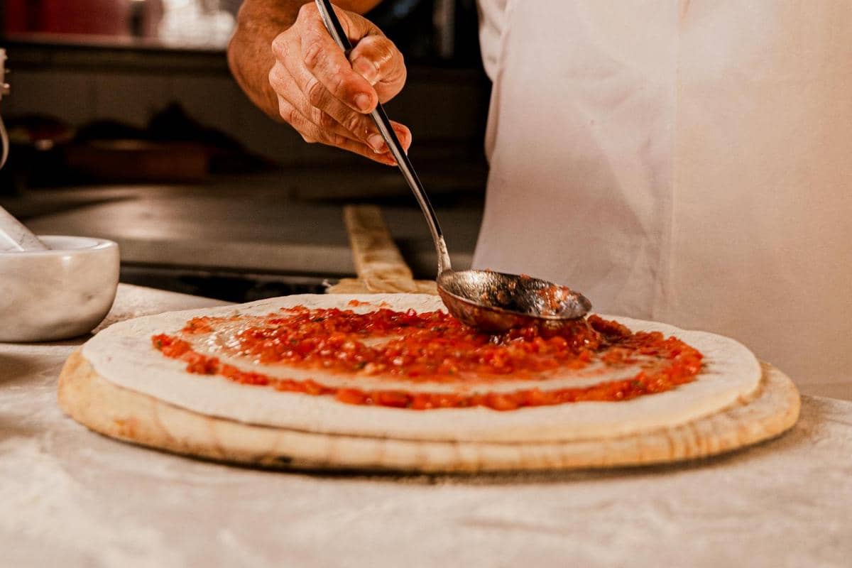 ilustrasi mengoleskan saus bolognese ke atas pizza