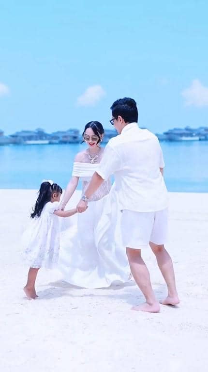 Nanda Arsyinta mengenakan gaun putih bermain di pantai bersama seorang pria dan anak kecil di bawah langit biru cerah.