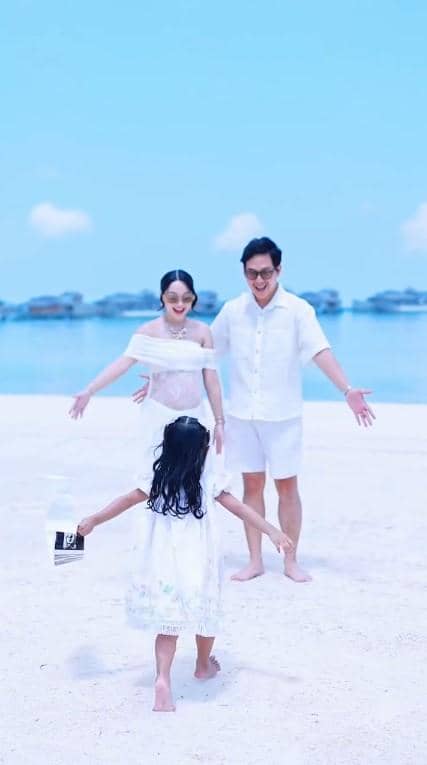Nanda Arsyinta bersama suami dan anak kecil mereka di pantai berpasir putih dengan latar laut biru yang tenang.