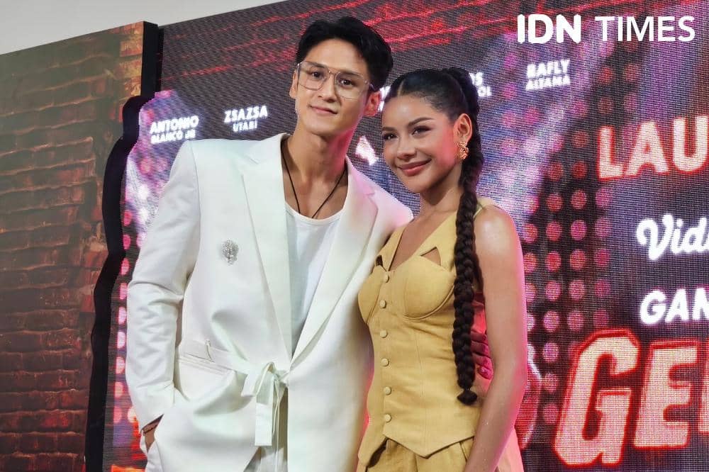 Seorang pria mengenakan setelan jas putih berdiri di samping seorang wanita bergaun kuning dengan kepangan panjang di sebuah acara di Jakarta.