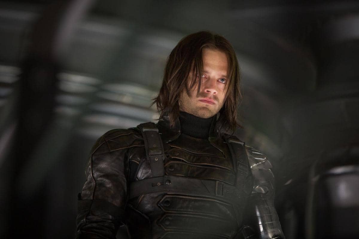 Bucky Barnes mengenakan pakaian tempur hitam dengan ekspresi serius di dalam ruangan berteknologi tinggi.